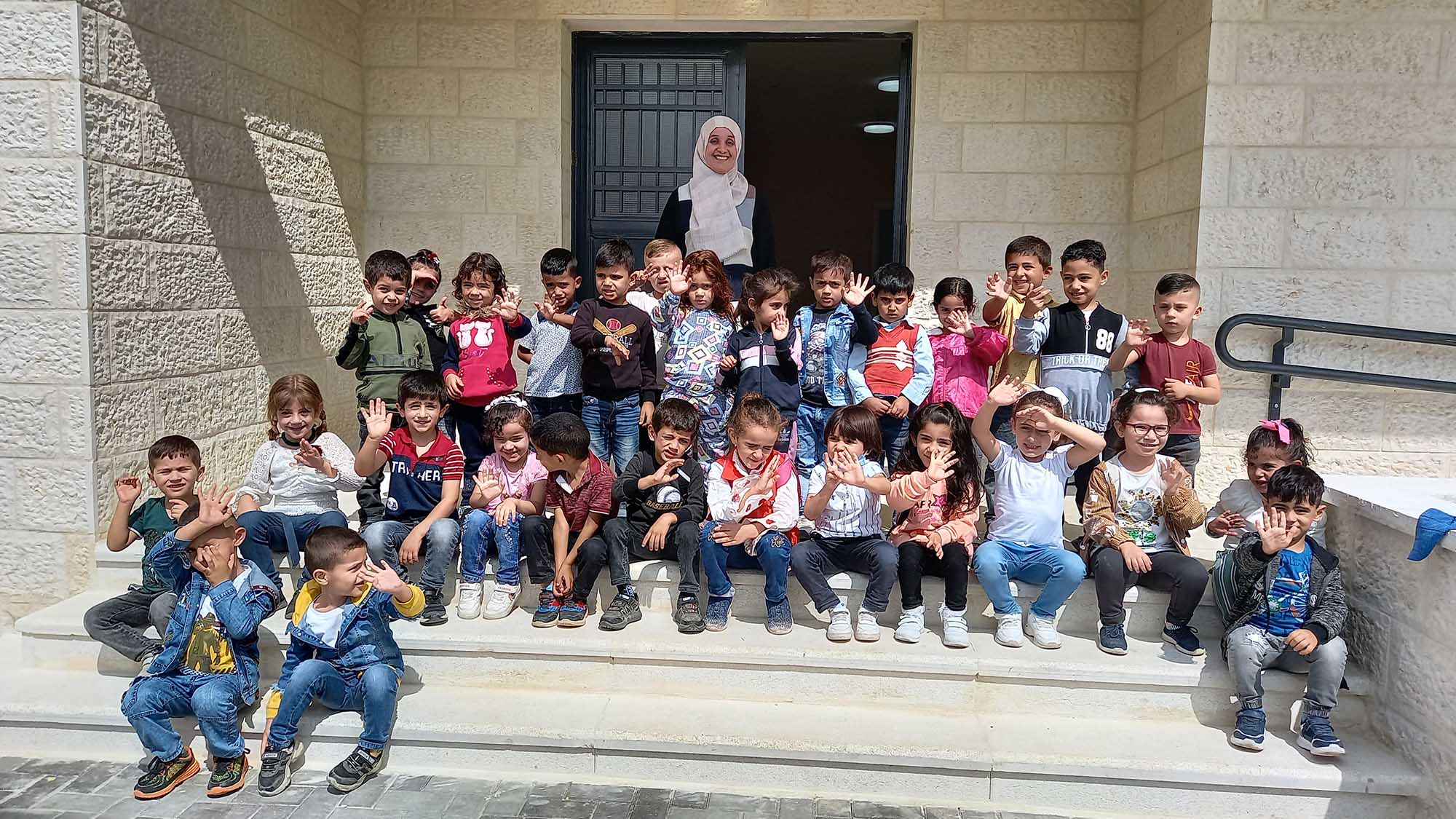 Preschool children sitting together on the steps of their kindergarten in As-Sammu, Palestine