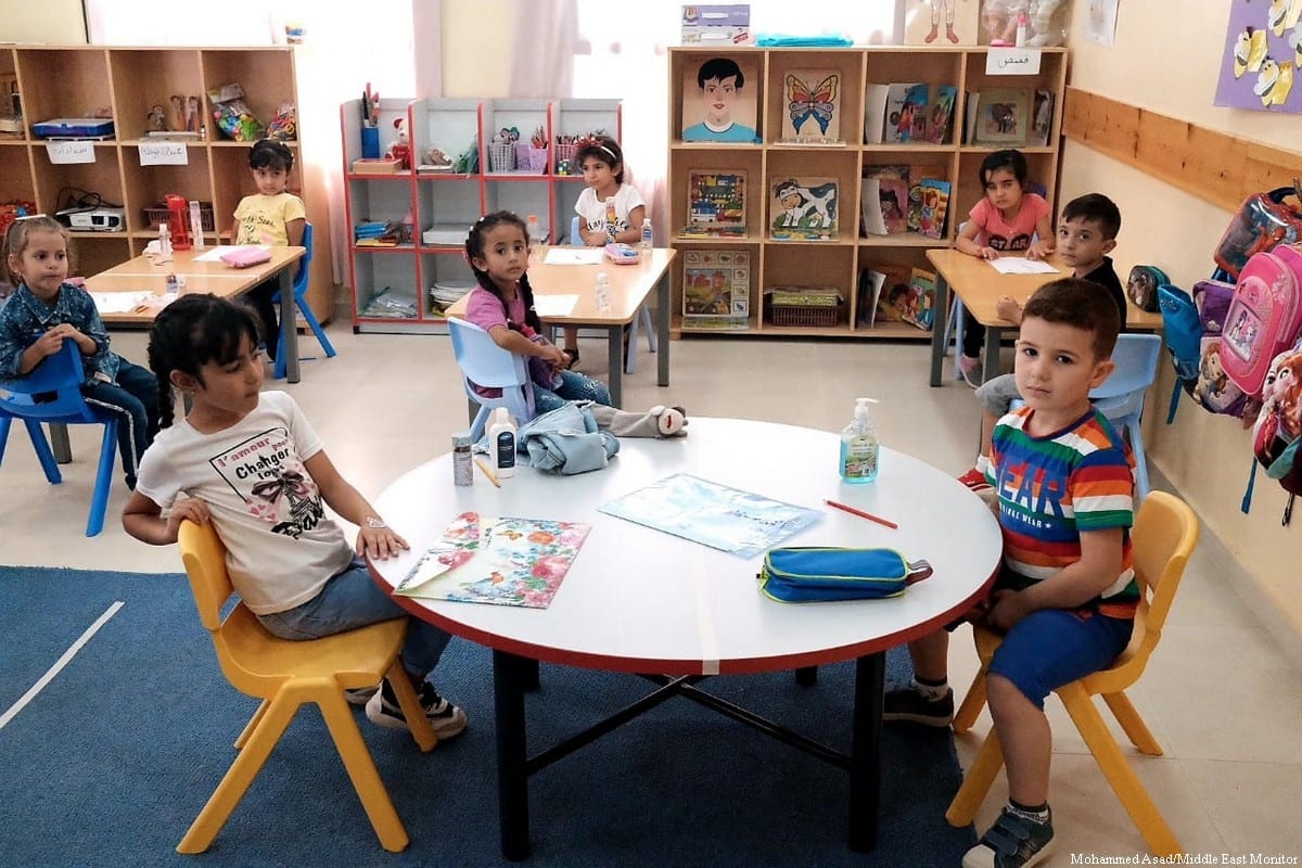 Preschoolers seated around low round tables in a classroom lined with books